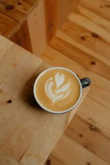 A high-angle close-up of a latte in a dark grey cup, featuring intricate white latte art on a light brown surface.