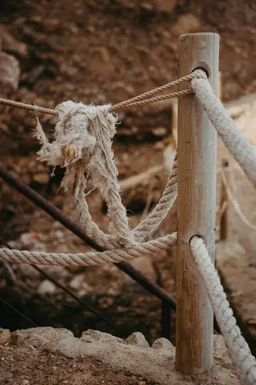 Detailní záběr světle hnědého dřevěného sloupku s několika silnými, krémově bílými lany svázanými kolem něj, tvořícími