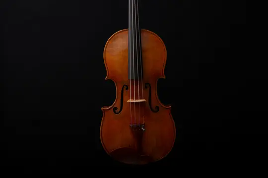 A classic wooden violin is positioned vertically against a plain black background, highlighting its rich brown tones and…