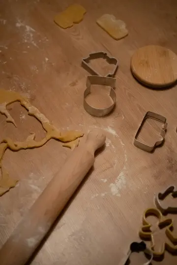 A high-angle shot of a wooden surface with cookie dough, flour, various metal cookie cutters, and a wooden rolling pin.