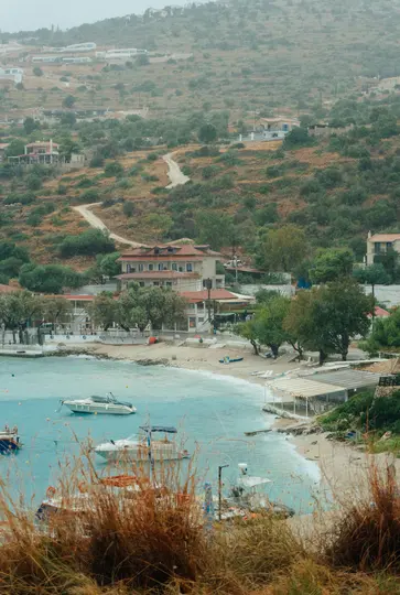 Μια υπερυψωμένη άποψη ενός παραθαλάσσιου χωριού με έναν ήρεμο κόλπο με πολλά σκάφη, μια αμμώδη παραλία και κτίρια κατά μήκος