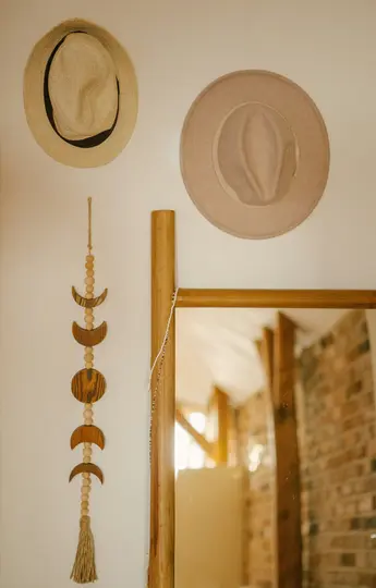 Due cappelli, uno di paglia e uno di feltro, sono appesi a un muro chiaro sopra una decorazione murale delle fasi lunari in