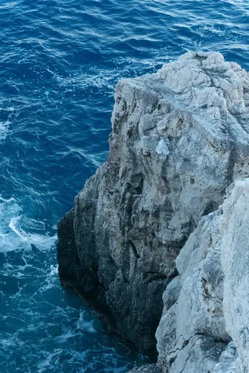 Una vista de primer plano, en ángulo alto, de una escarpada pared de acantilado de color gris claro que se encuentra con el