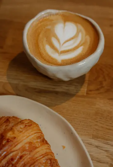 Primo piano, vista dall'alto di una tazza in ceramica bianca di latte con un disegno a forma di cuore in latte art, accanto a