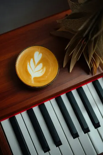 A top-down view of a cup of latte with white latte art, a fanned-out book, and black and white piano keys.