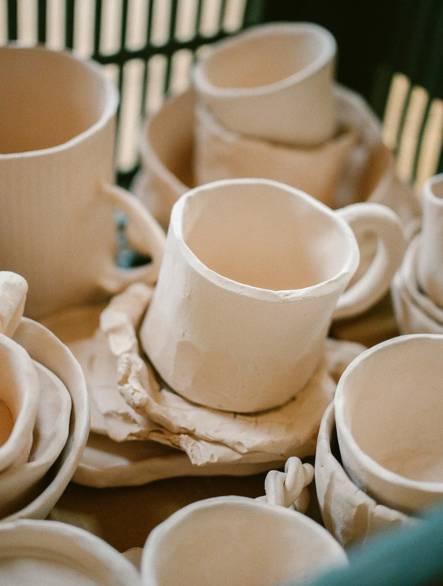 Zbliżenie, ujęcie z góry kilku ręcznie robionych, nieszkliwionych ceramicznych filiżanek i spodków w różnych stadiach