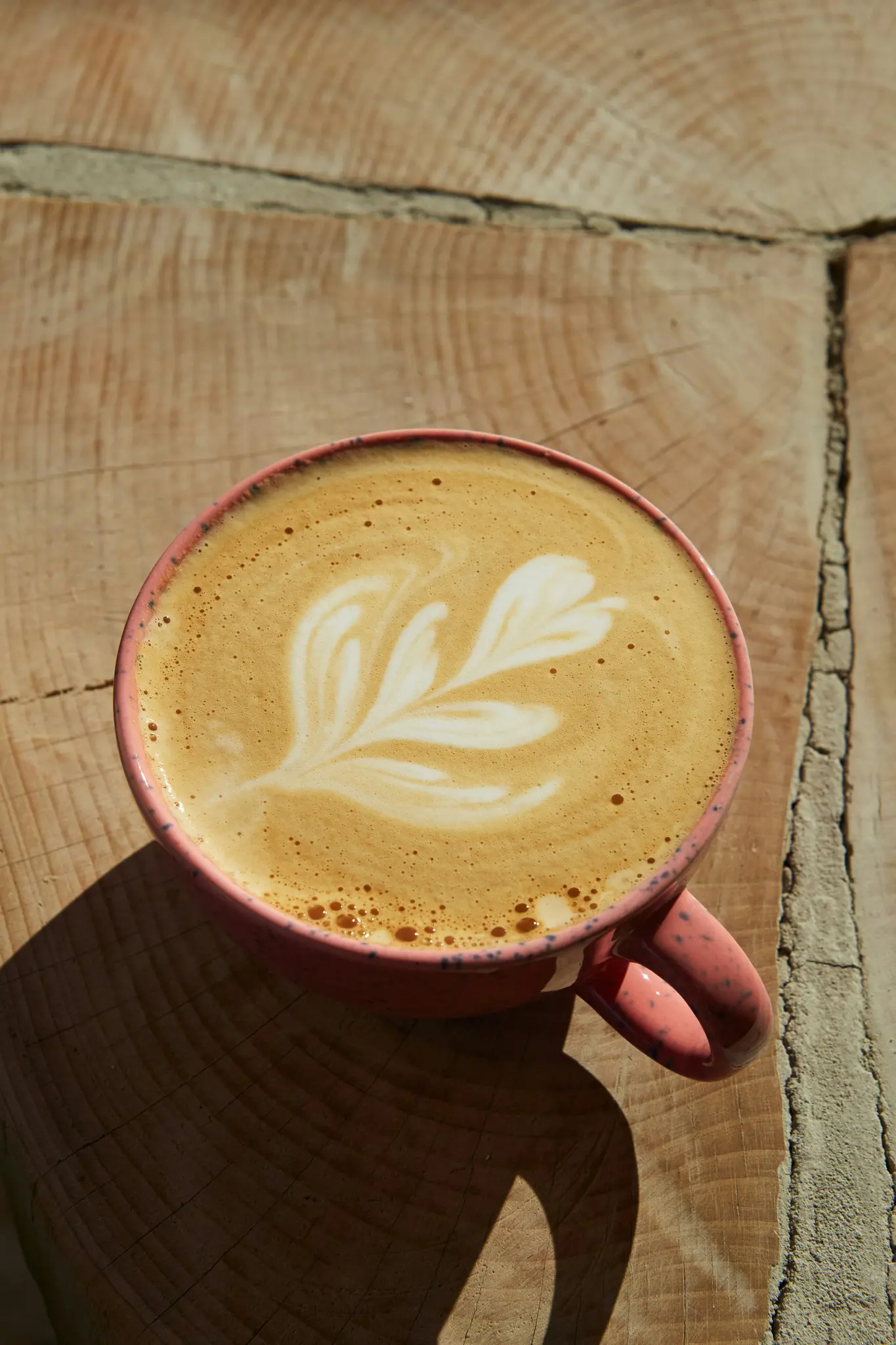 Een close-up, van bovenaf genomen, van een roze gevlekte mok gevuld met een latte, met ingewikkelde witte schuimkunst.
