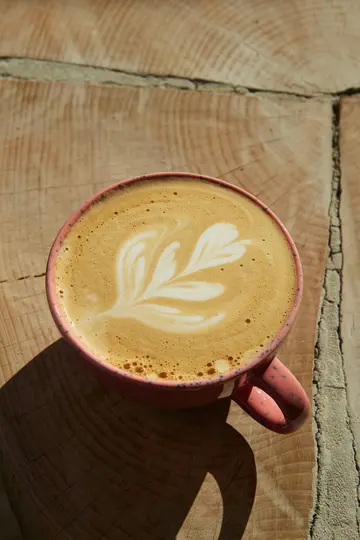 Detailní záběr z ptačí perspektivy na růžový, skvrnitý hrnek s latte a složitým bílým pěnovým uměním.