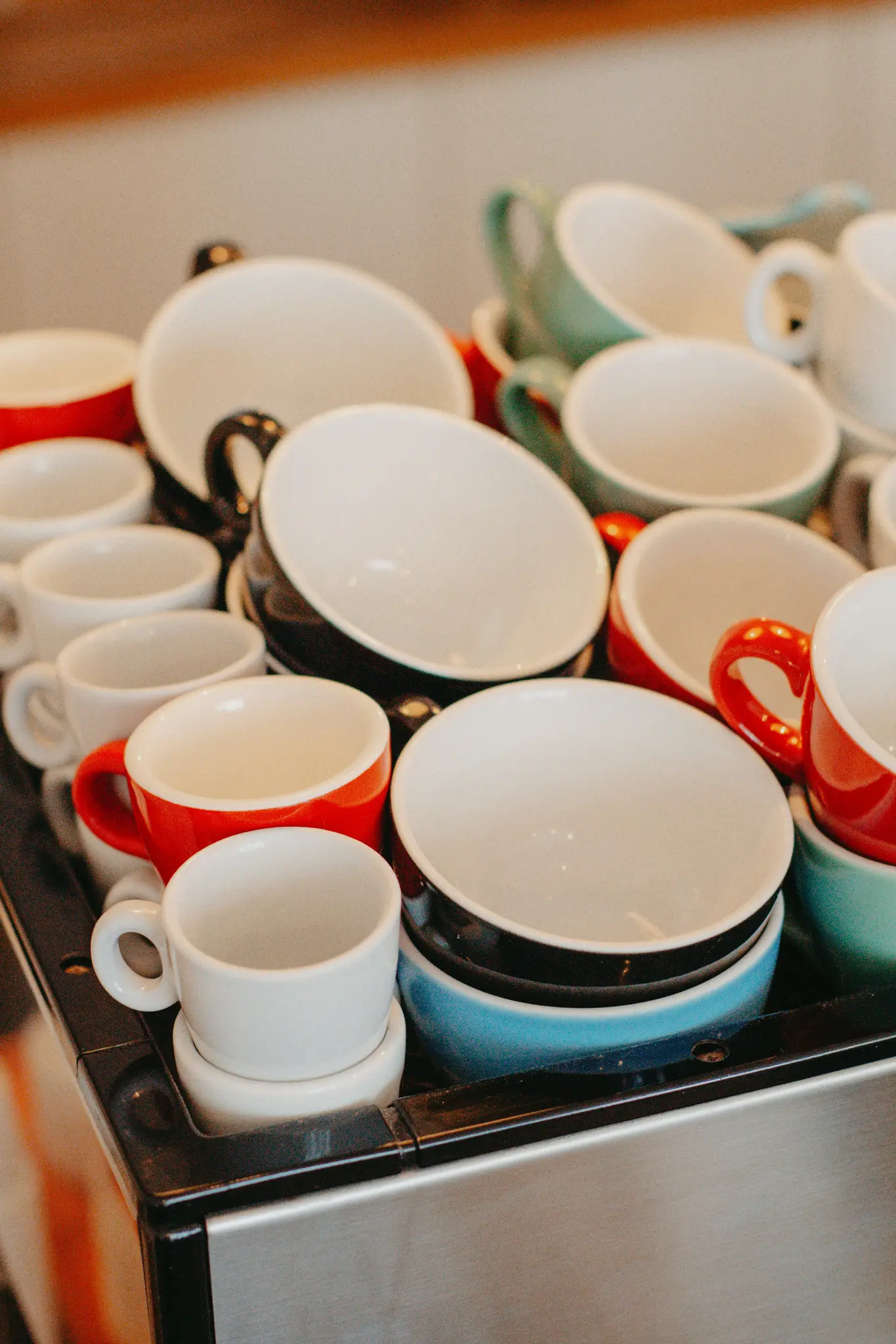 Una toma de primer plano de numerosas tazas y cuencos de café en varios colores, incluyendo blanco, rojo, negro, turquesa y