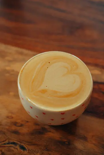 Vista ravvicinata, dall'alto, di una tazza in ceramica bianca con piccoli cuori rossi, contenente un latte con un disegno di