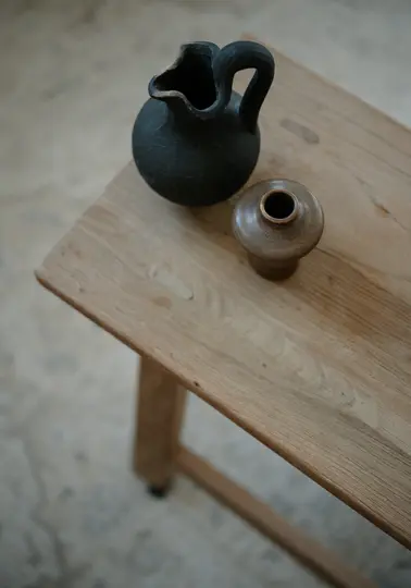 Una toma cenital muestra dos vasijas de cerámica sobre una mesa de madera clara. Una es una jarra gris oscuro, la otra una