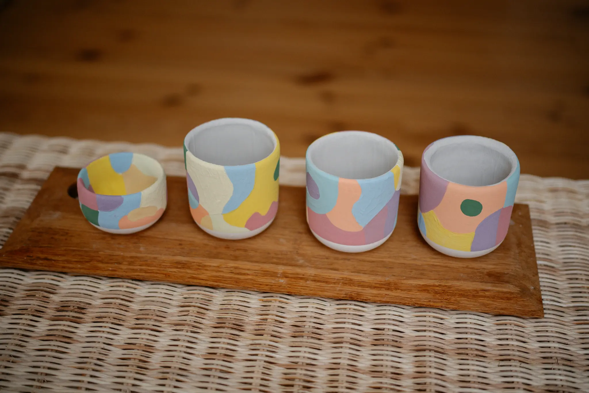 Quatre petites tasses en céramique blanche sont peintes à la main avec des formes abstraites pastel en bleu clair, jaune