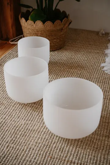 Tre ciotole bianche in vetro smerigliato di varie dimensioni sono disposte su un tappetino intrecciato marrone chiaro. Una