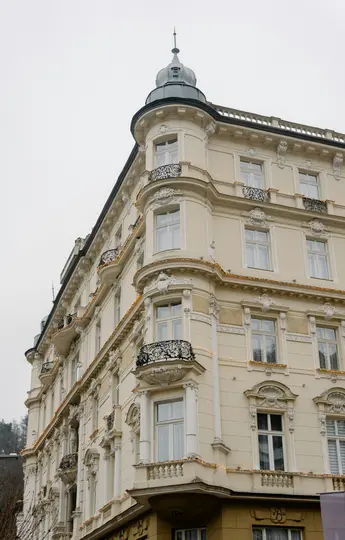 Záběr z nízkého úhlu na ozdobnou krémovou budovu s tmavě šedou věží v rohu. Dekorativní balkony a provázek...
