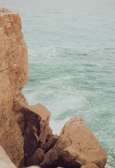 Μια κοντινή λήψη από ψηλά, μιας ανάγλυφης, κοκκινωπής-καφέ βραχώδους όψης στα αριστερά, που συναντά το γαλαζοπράσινο και