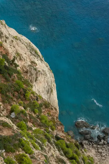 Una vista aérea captura un acantilado escarpado y de color claro cubierto de vegetación verde y marrón, que se encuentra con
