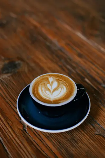 Ένα σκούρο μπλε φλιτζάνι και πιατάκι με ένα latte με σχέδιο αφρού σε σχήμα καρδιάς, που κάθεται σε ένα ρουστίκ ξύλινο