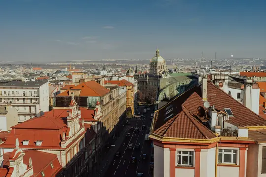 Pohled na město z ptačí perspektivy ukazující četné budovy s červenými a oranžovými taškovými střechami, ulici s auty a