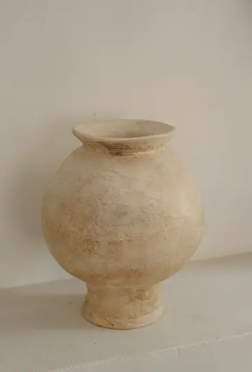 Una maceta de cerámica redonda de color beige claro con un borde acampanado y una superficie texturizada se encuentra sobre