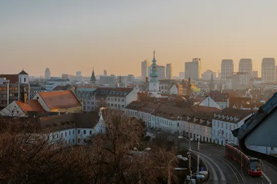 Vyvýšený pohled na město za zlaté hodinky, ukazující směs historických budov s červenými střechami a moderních mrakodrapů.