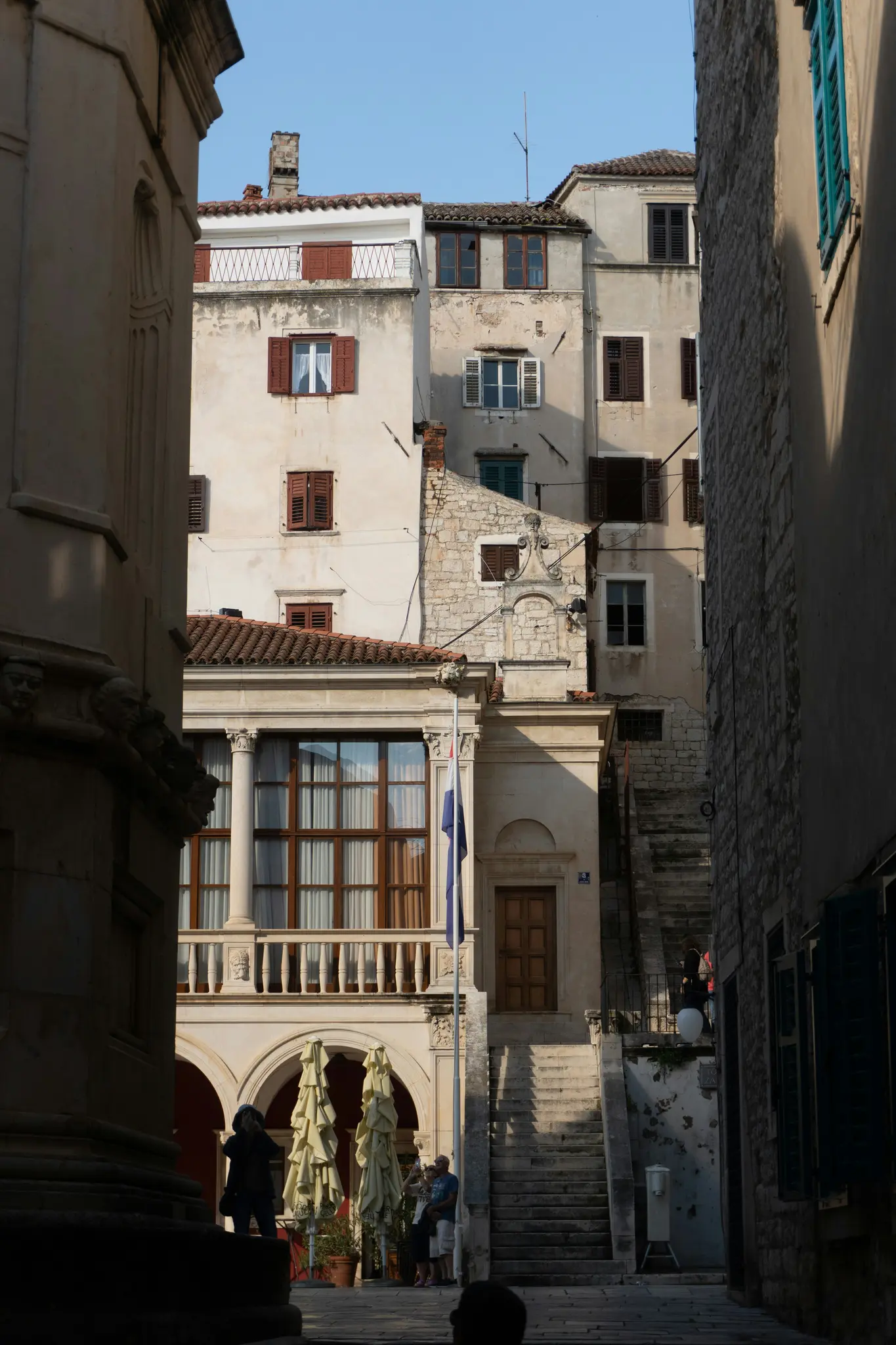 Μια κάθετη λήψη ενός στενού δρόμου σε μια ιστορική πόλη. Παλιά κτίρια με παράθυρα με κόκκινα παντζούρια πλαισιώνουν το δρόμο