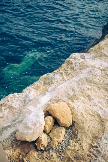 Un primer plano a vista de pájaro de una escarpada y clara costa rocosa que se encuentra con aguas oceánicas de color azul