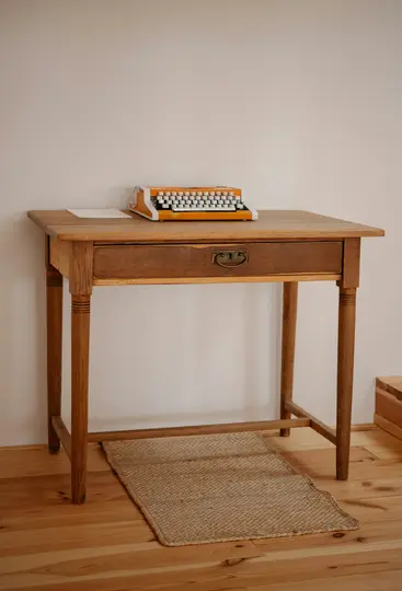 Una máquina de escribir vintage de color naranja brillante y blanco descansa sobre un escritorio de madera sencillo. Una