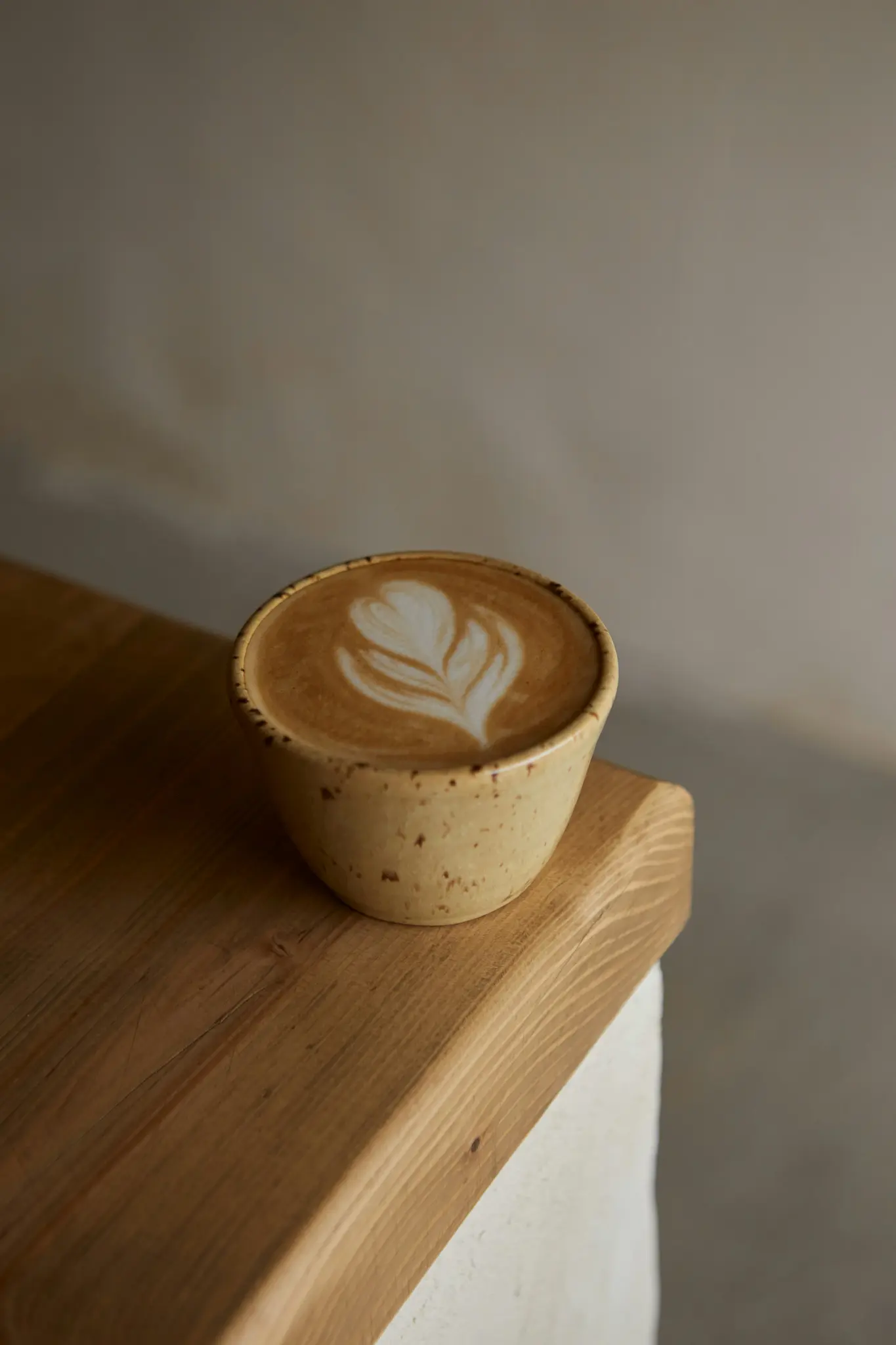 Une tasse en céramique beige tachetée remplie d'un latte avec un art latte blanc complexe est posée sur une surface en bois