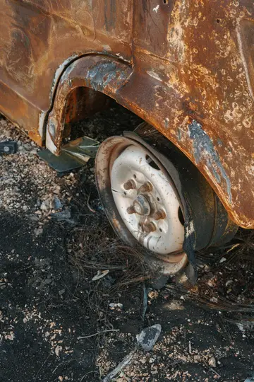 O fotografie de aproape a unui noroi de roată de vehicul grav ruginit și ars, cu o roată albă deteriorată și un cauciuc topit