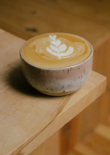 A close-up shot of a ceramic cup filled with a latte, featuring a delicate white latte art design on its surface. The cup…