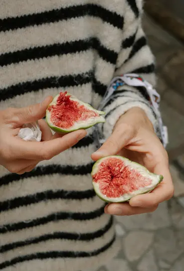 Detailní záběr dvou rukou držících dvě poloviny čerstvé fiky, odhalující její jasně červený vnitřek plný semen a zelenou