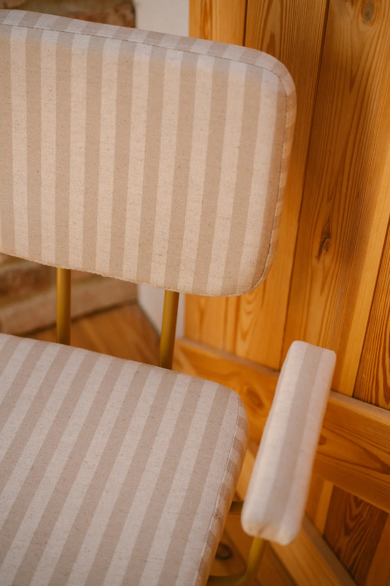 Nahaufnahme eines Stuhls mit beige- und cremefarbenen vertikalen Streifen und hellbrauner Holzvertäfelung dahinter.