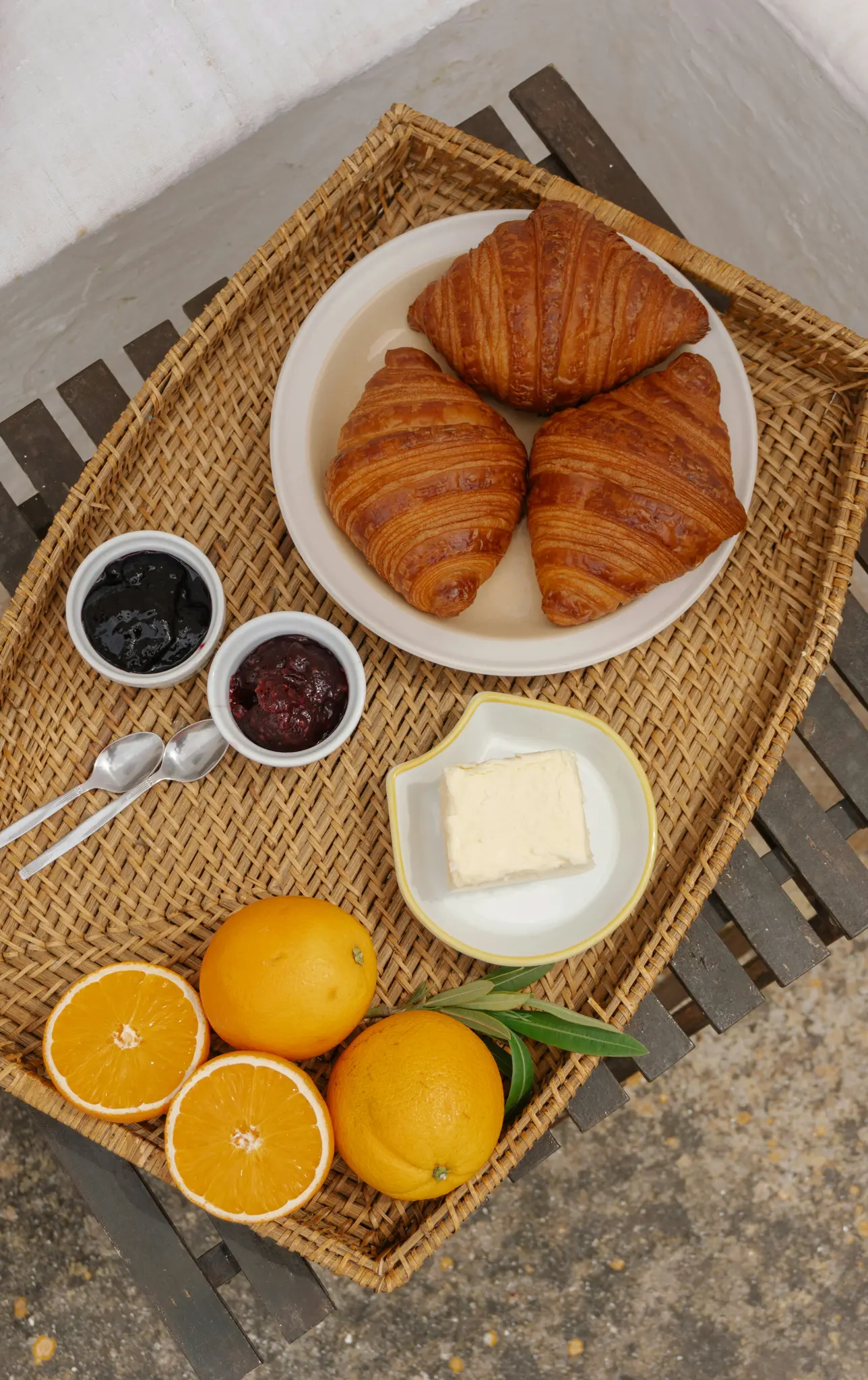 En ovanifrån-bild av en korgbricka med tre gyllenbruna croissanter, två små skålar med sylt, en smörbytta och fyra…