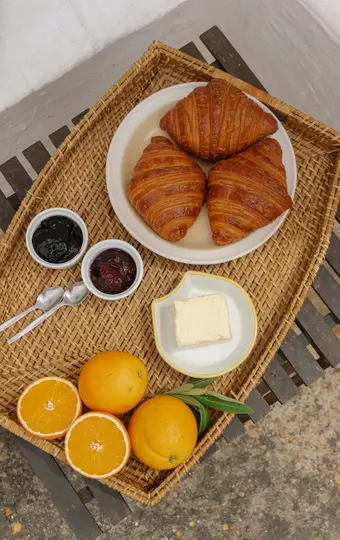 Una ripresa dall'alto di un vassoio di vimini con tre croissant dorati, due ciotoline di marmellata, un contenitore di burro