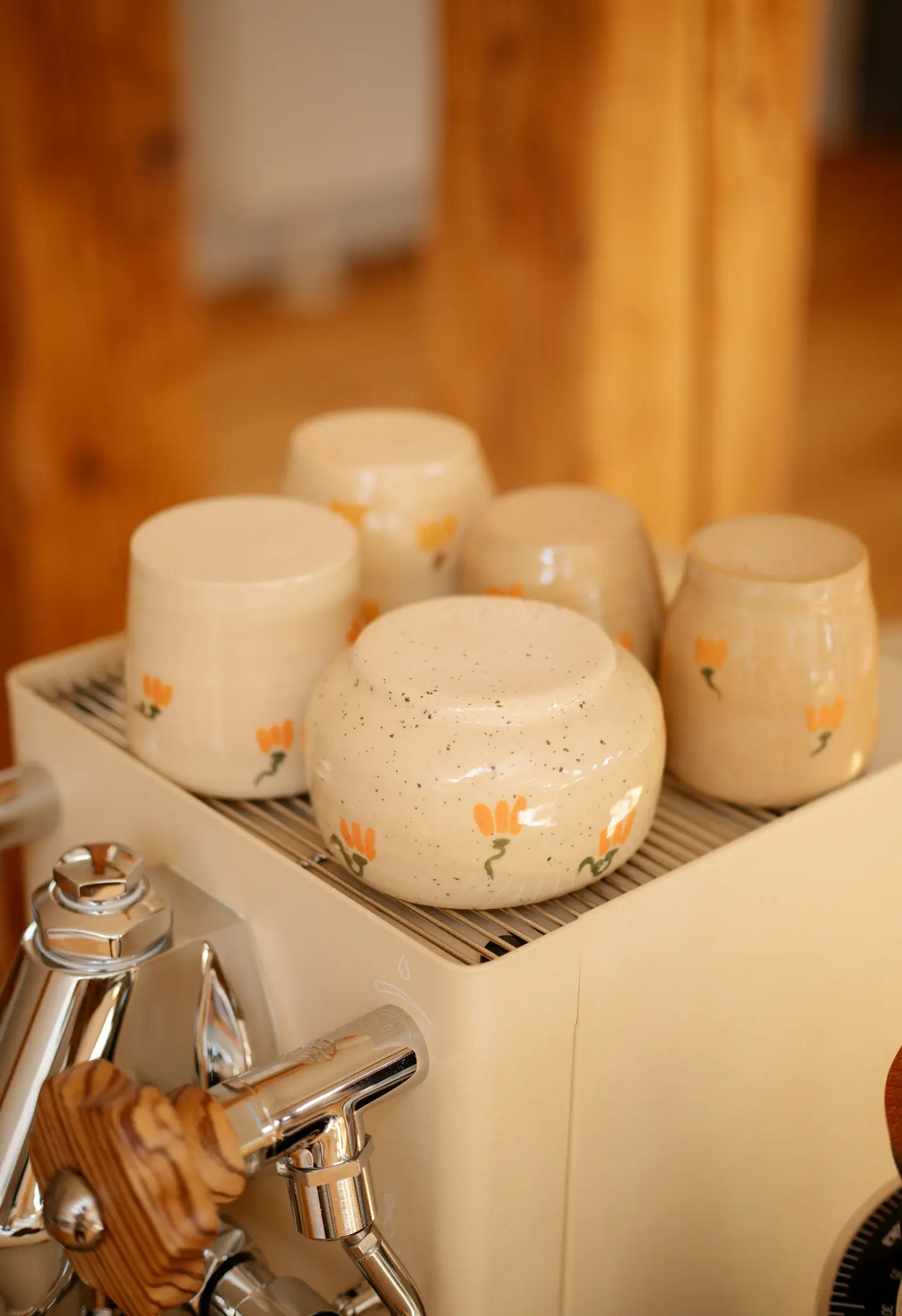 Un gros plan montre cinq tasses en céramique de couleur crème, chacune décorée de petits motifs floraux orange, séchant sur