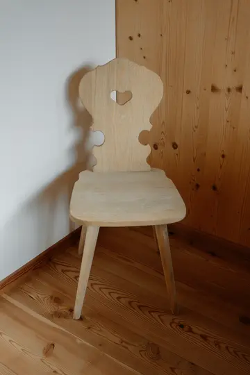 Una silla de madera clara con un recorte en forma de corazón en el respaldo se encuentra en una esquina. La silla está hecha