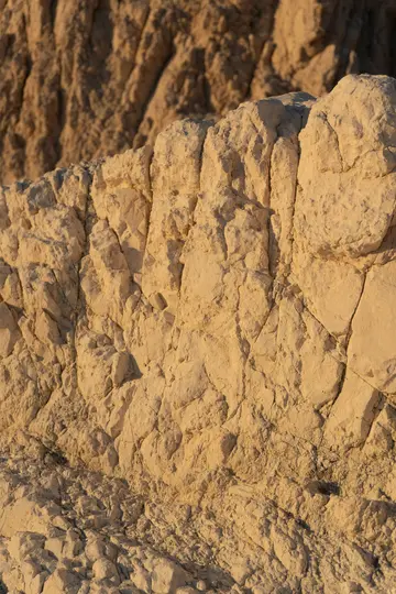 Detailní záběr drsné skalní formace, osvětlené teplým zlatým světlem, které zdůrazňuje její praskliny a nerovný povrch.