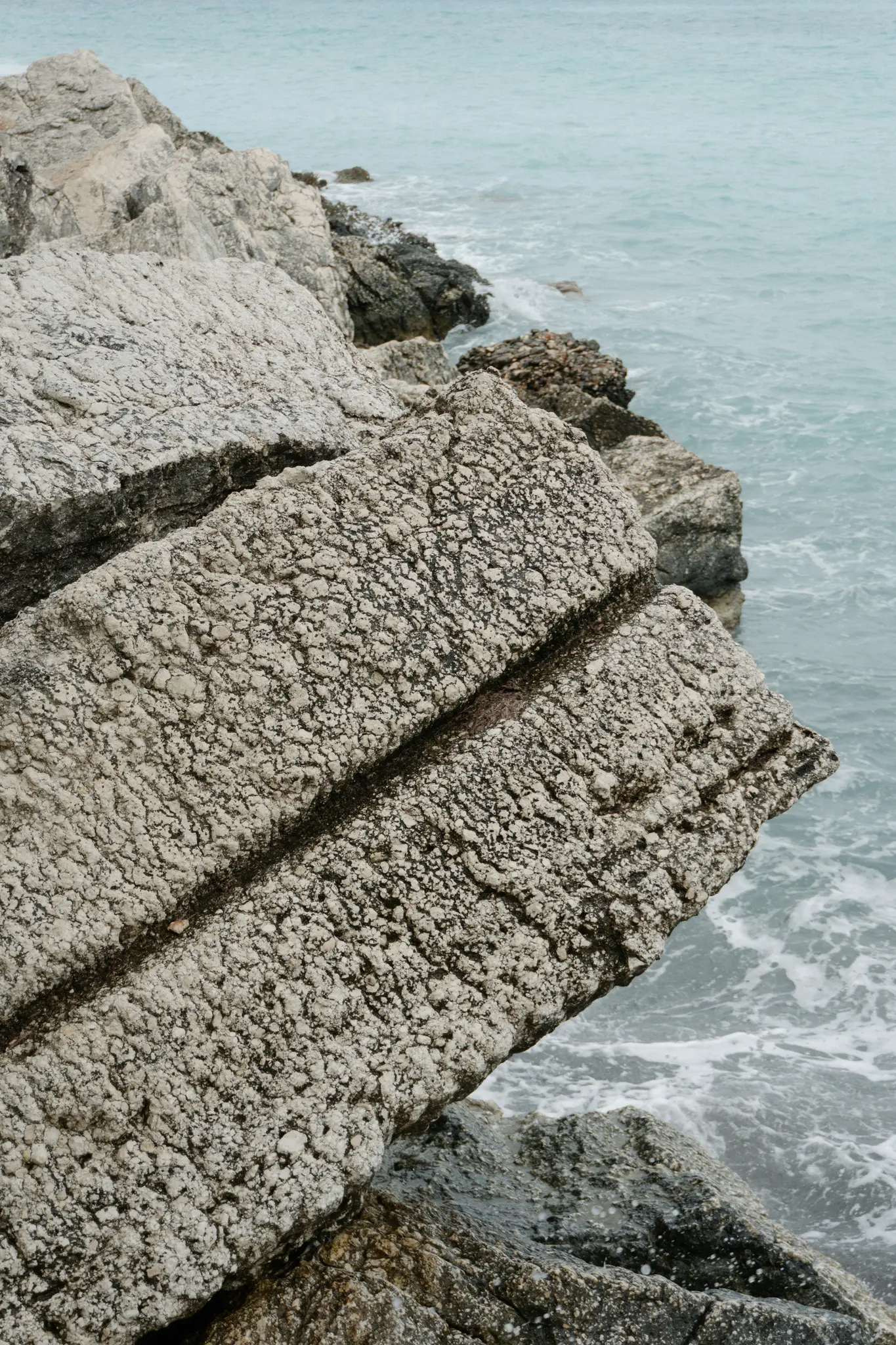 Una vista ravvicinata di formazioni rocciose grigio chiaro e molto texturizzate lungo la costa, con il mare azzurro sullo