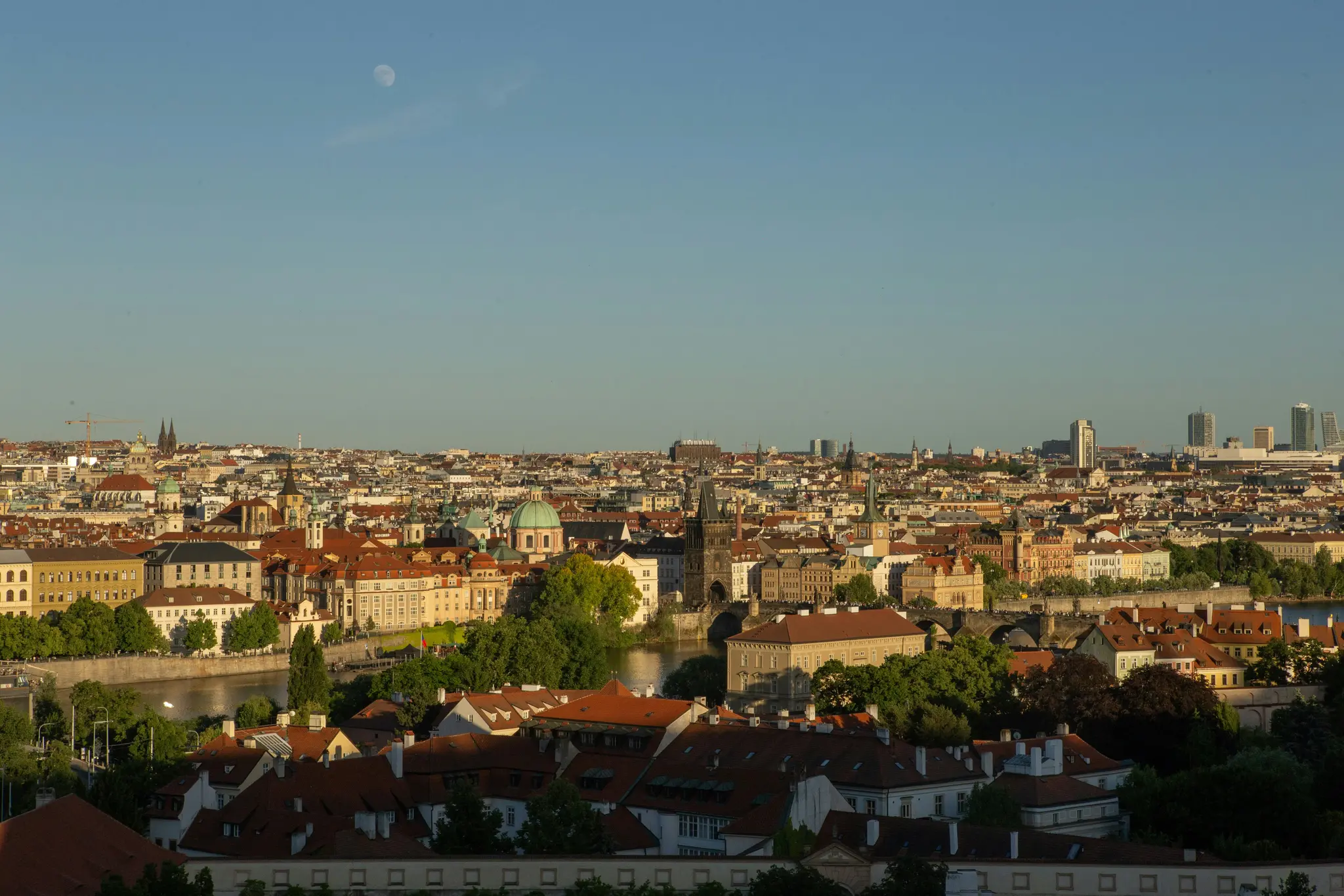 Une vue aérienne d'une ville tentaculaire avec des bâtiments aux toits rouges, une rivière qui la traverse et une lune