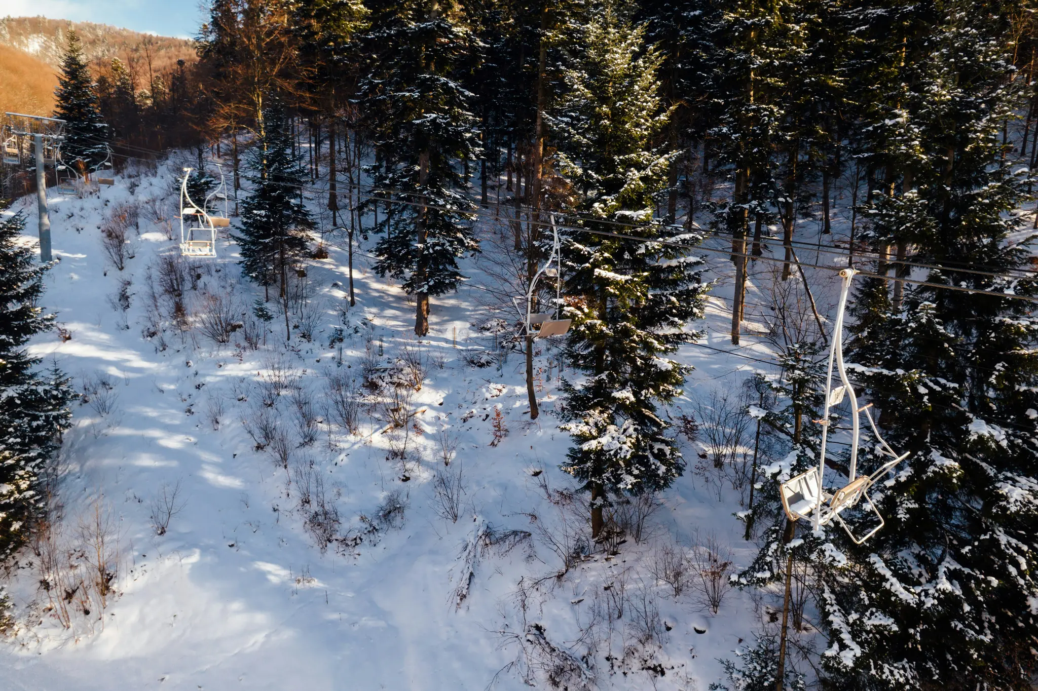 Une vue aérienne montre un téléski avec des chaises vides se déplaçant sur une pente de montagne enneigée bordée d'arbres à