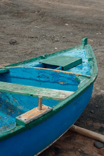 Una toma de primer plano, en ángulo alto, de una pequeña barca de madera vieja pintada en azul y verde descascarillado
