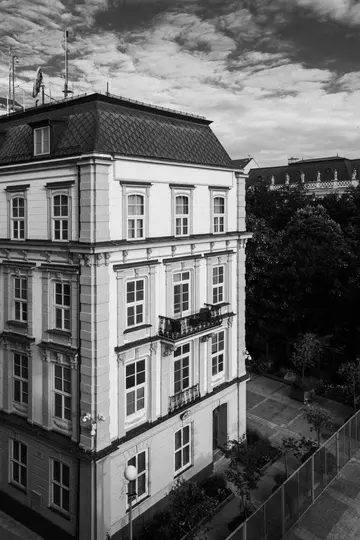 Uno scatto in bianco e nero, dall'alto, di un edificio ornato con tetto mansardato, molteplici finestre e un piccolo balcone.