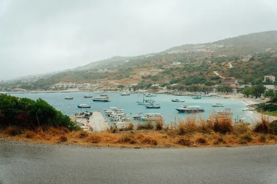 Μια υπερυψωμένη θέα ενός ήρεμου κόλπου γεμάτου πολυάριθμα σκάφη, περιτριγυρισμένο από πράσινους και καφέ λόφους με κτίρια.