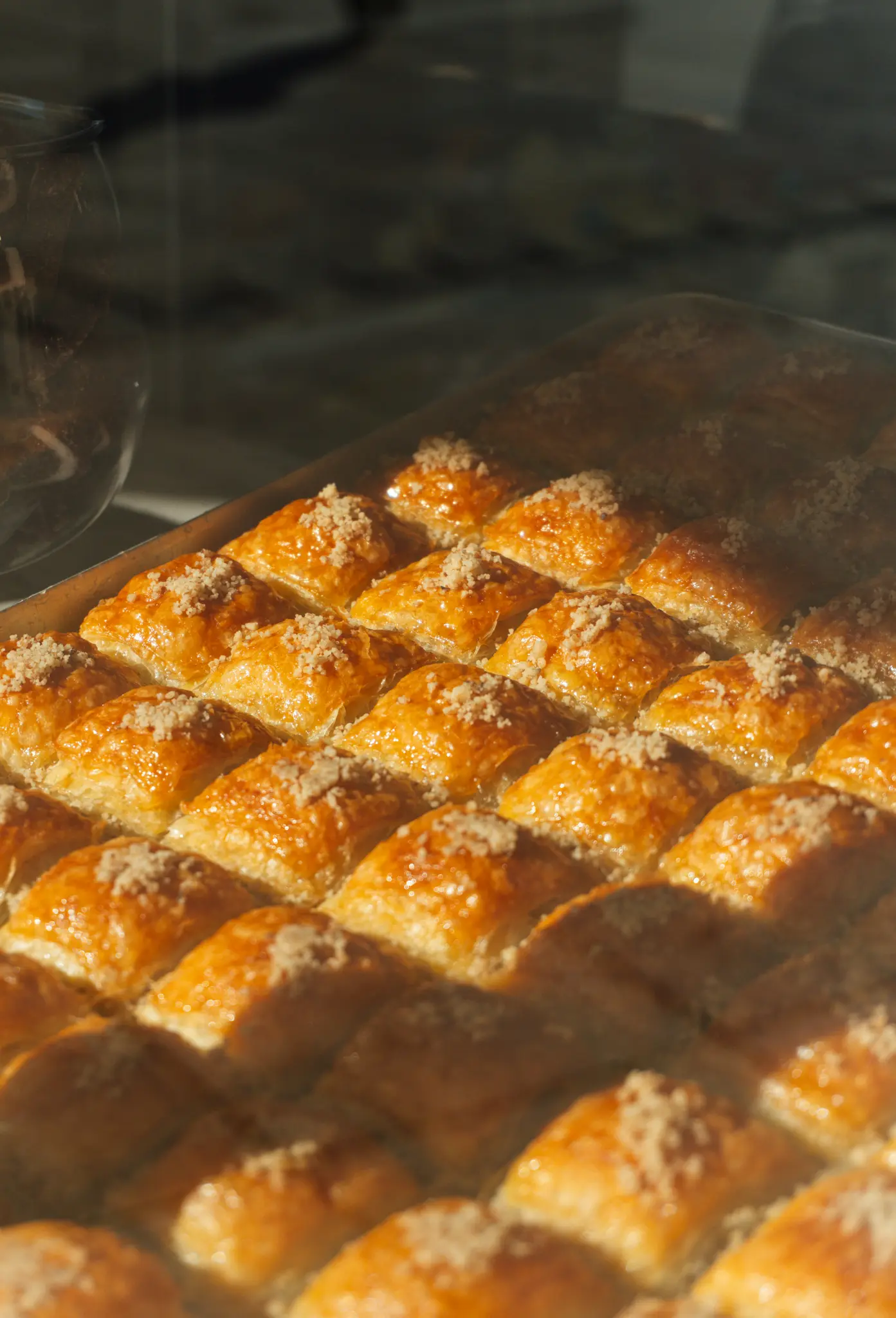 Detailný záber na podnos plný početných kosoštvorcových kúskov zlatohnedej baklavy posypaných nasekanými orechmi.