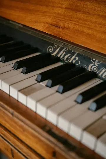 Vista ravvicinata, leggermente angolata, dei tasti bianchi e neri di un vecchio pianoforte, con una calda cassa in legno.