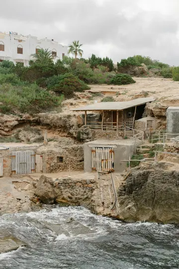 Θέα μιας βραχώδους ακτογραμμής με πολλά μικρά, ρουστίκ κτίρια ενσωματωμένα στους βράχους και ένα λευκό κτίριο στο...