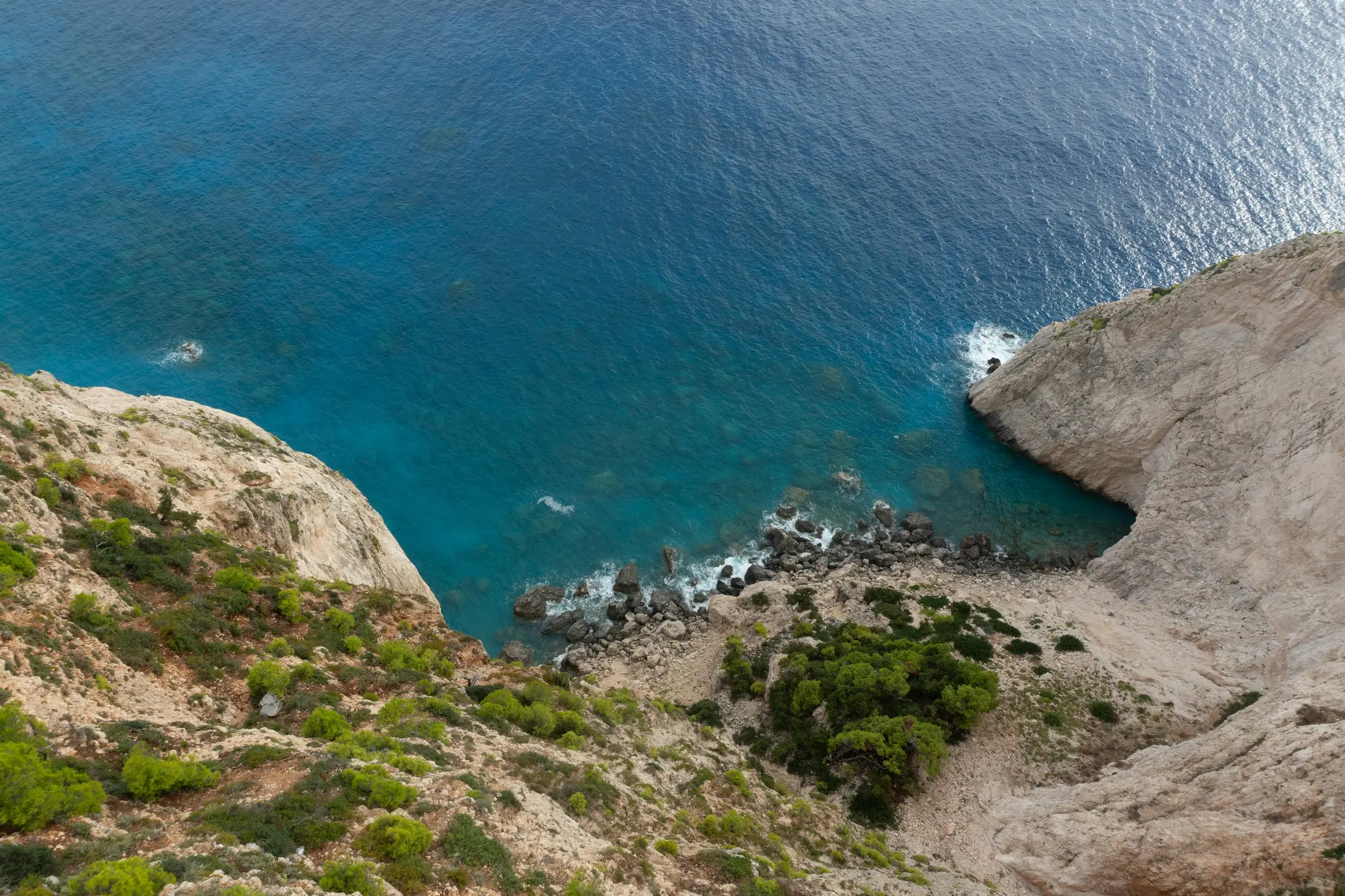 Μια εναέρια λήψη δείχνει μια τραχιά ακτογραμμή με απότομους, ανοιχτόχρωμους καφέ βράχους καλυμμένους με πράσινους θάμνους