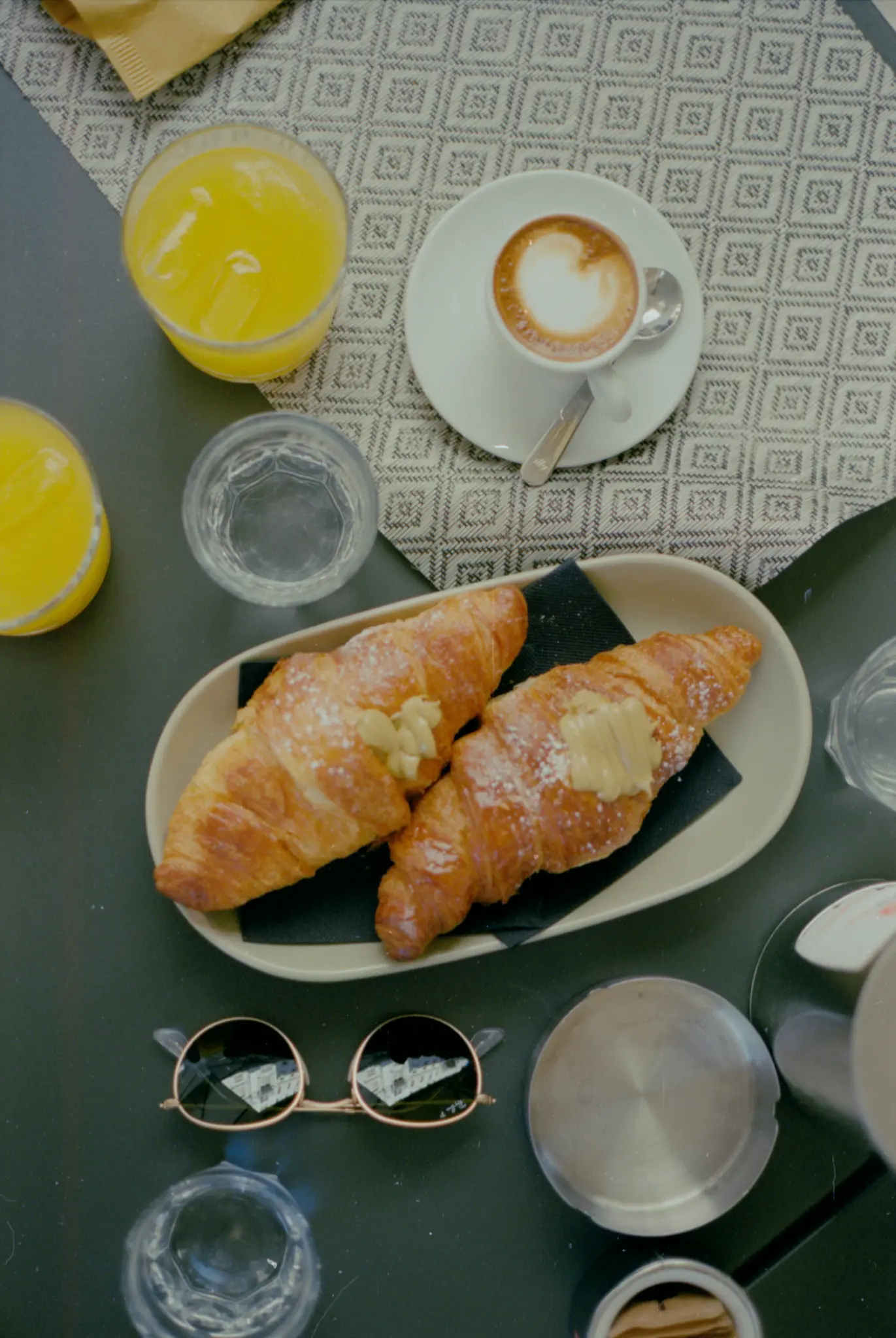 Une vue de dessus d'une table de petit-déjeuner avec deux croissants saupoudrés de sucre glace et de crème, une tasse de café