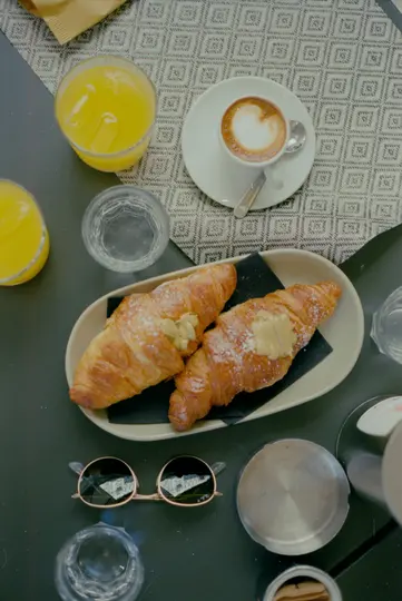 Pohled shora na snídaňový stůl se dvěma croissanty s moučkovým cukrem a smetanou, šálkem kávy s latte art...