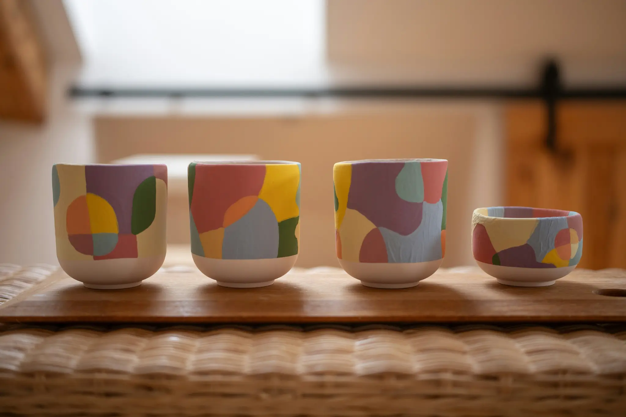 Quatre tasses en céramique de tailles variées, chacune ornée de motifs abstraits et colorés, reposent sur un plateau en bois